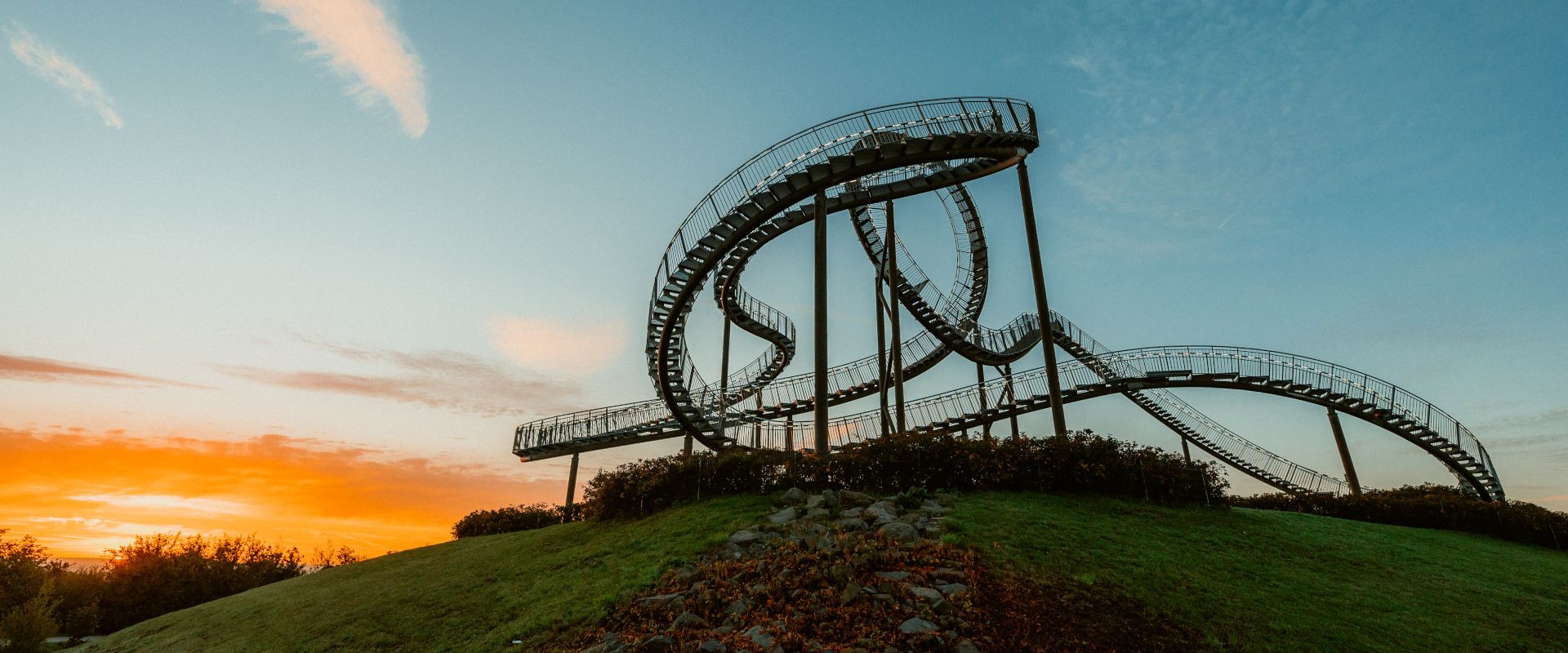 Seitliche Ansicht einer achterbahnählichen Skulptur auf der Heinrich-Hildebrand-Höhe in Duisburg bei Sonnenuntergang 