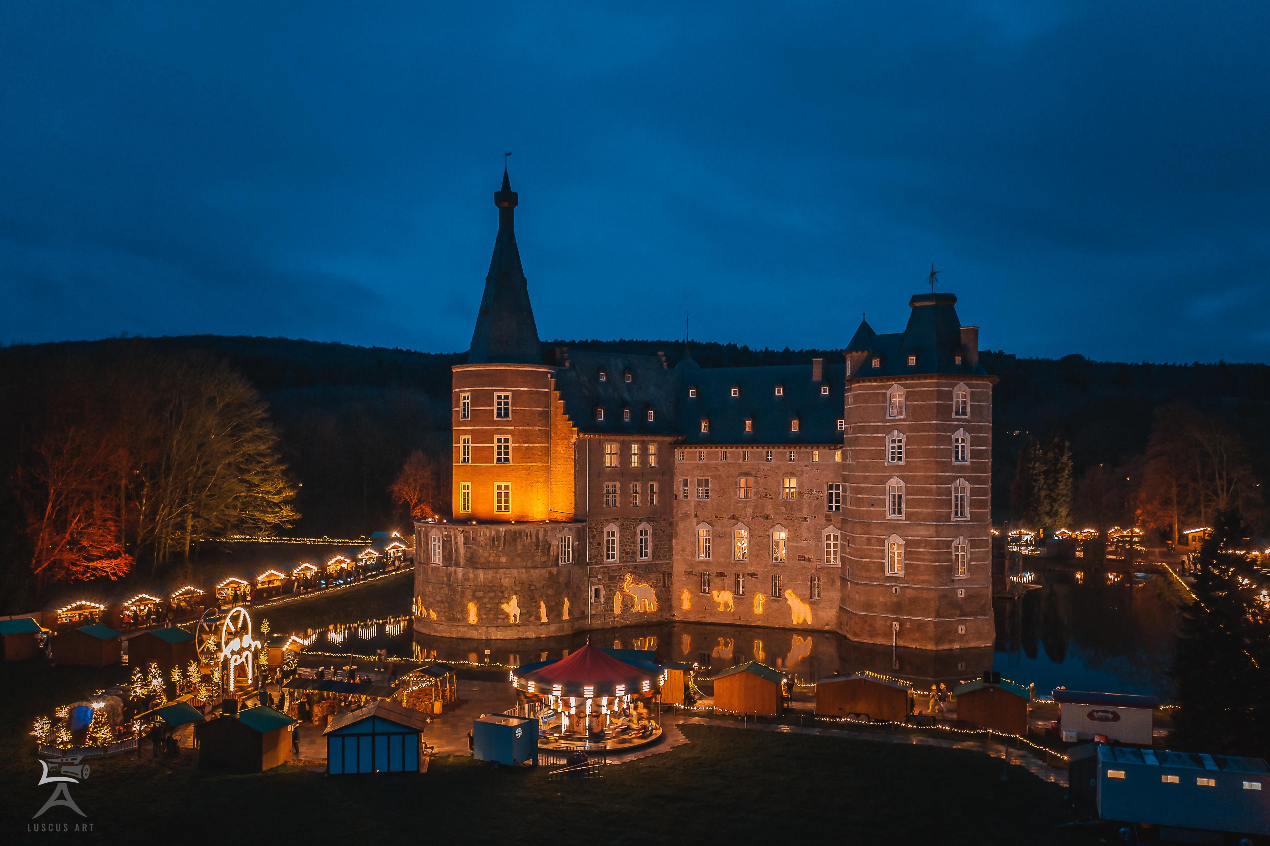 Merode Castle at night, festively illuminated with Christmas market stalls in the foreground.