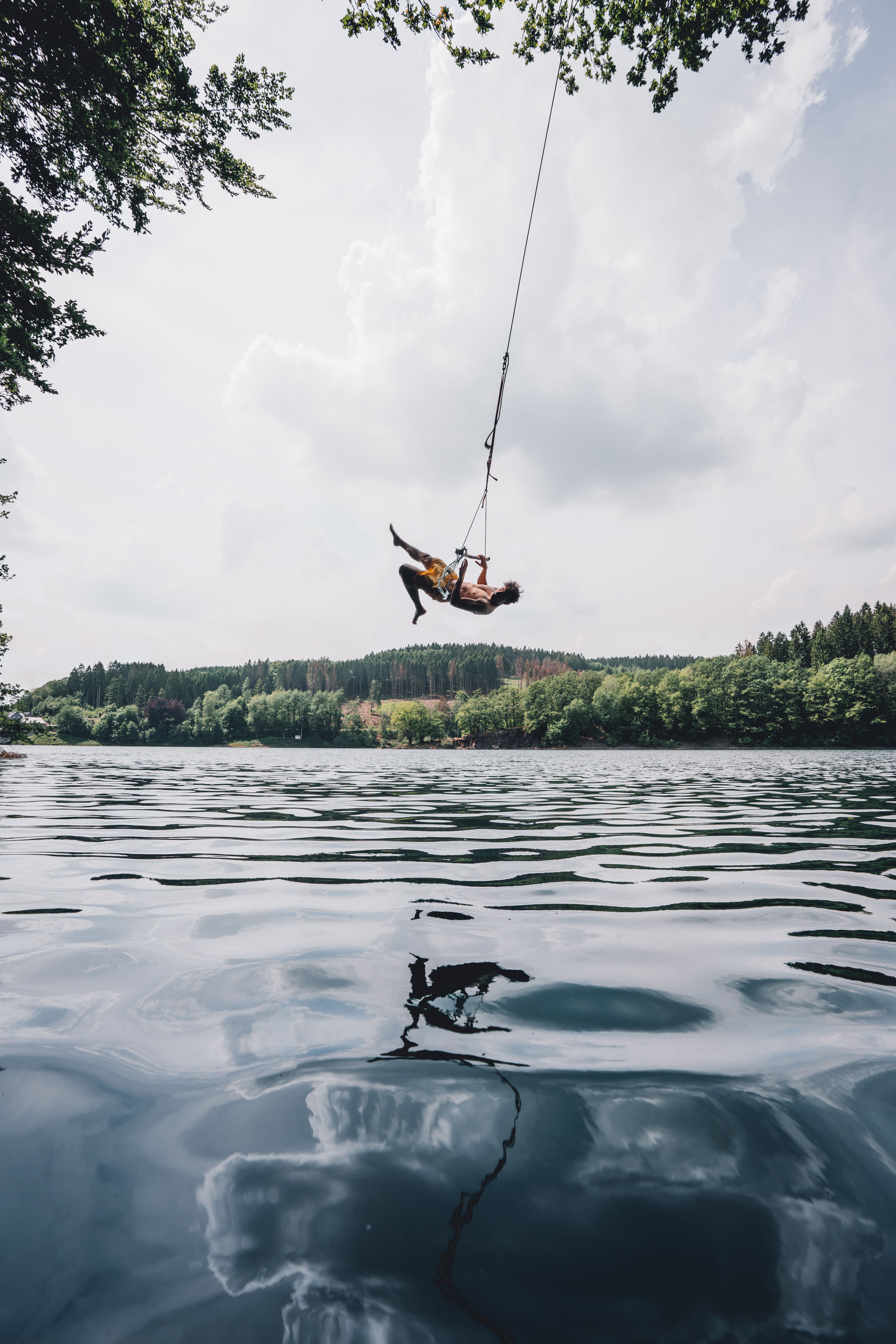 A person swings on a swing over the water of the Aggertal Reservoir, with a wooded shore in the background.