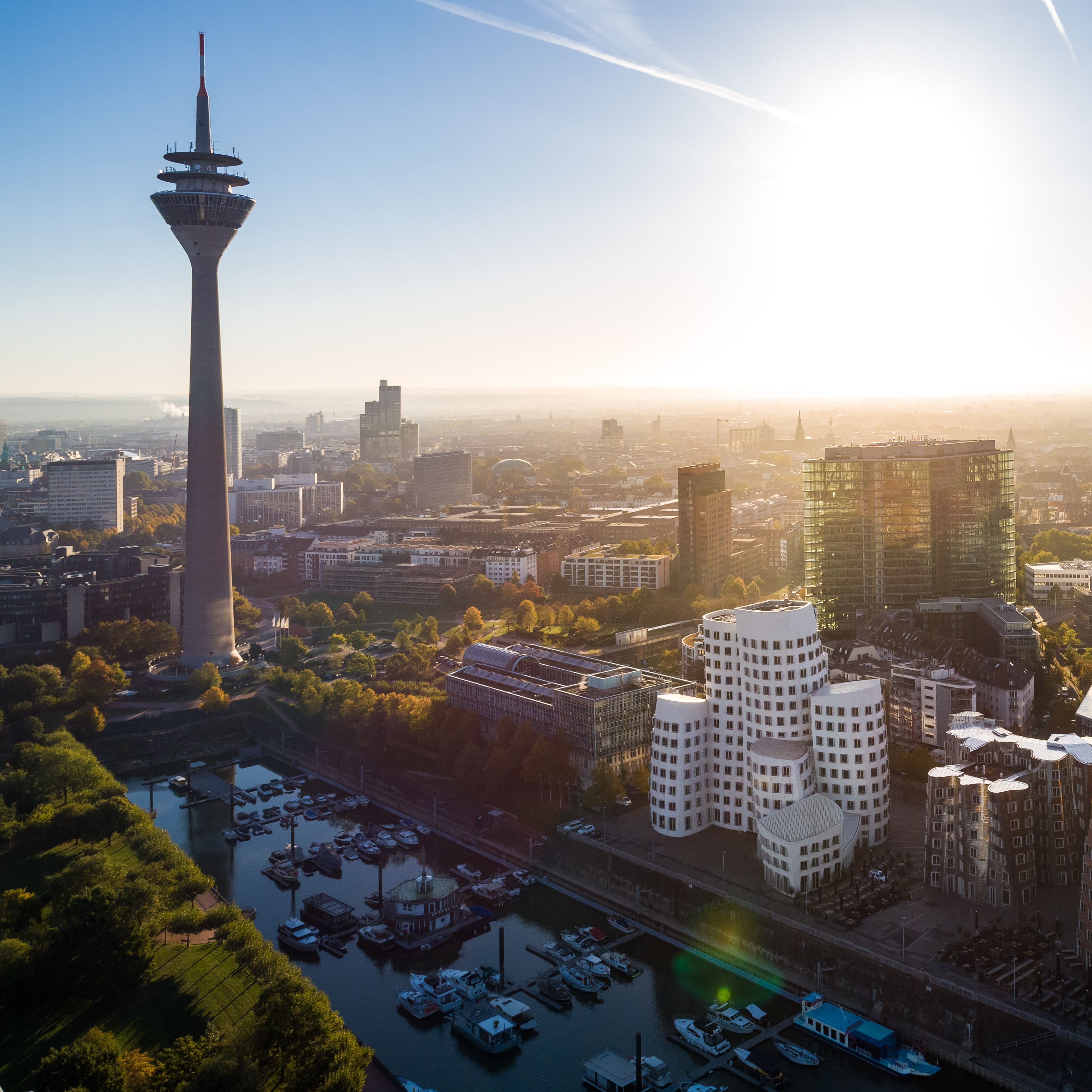 Sonne steht am Himmel über Düsseldorf, im Vordergrund sind Hafenbecken, Gehry-Bauten und Fernsehtum zu sehen