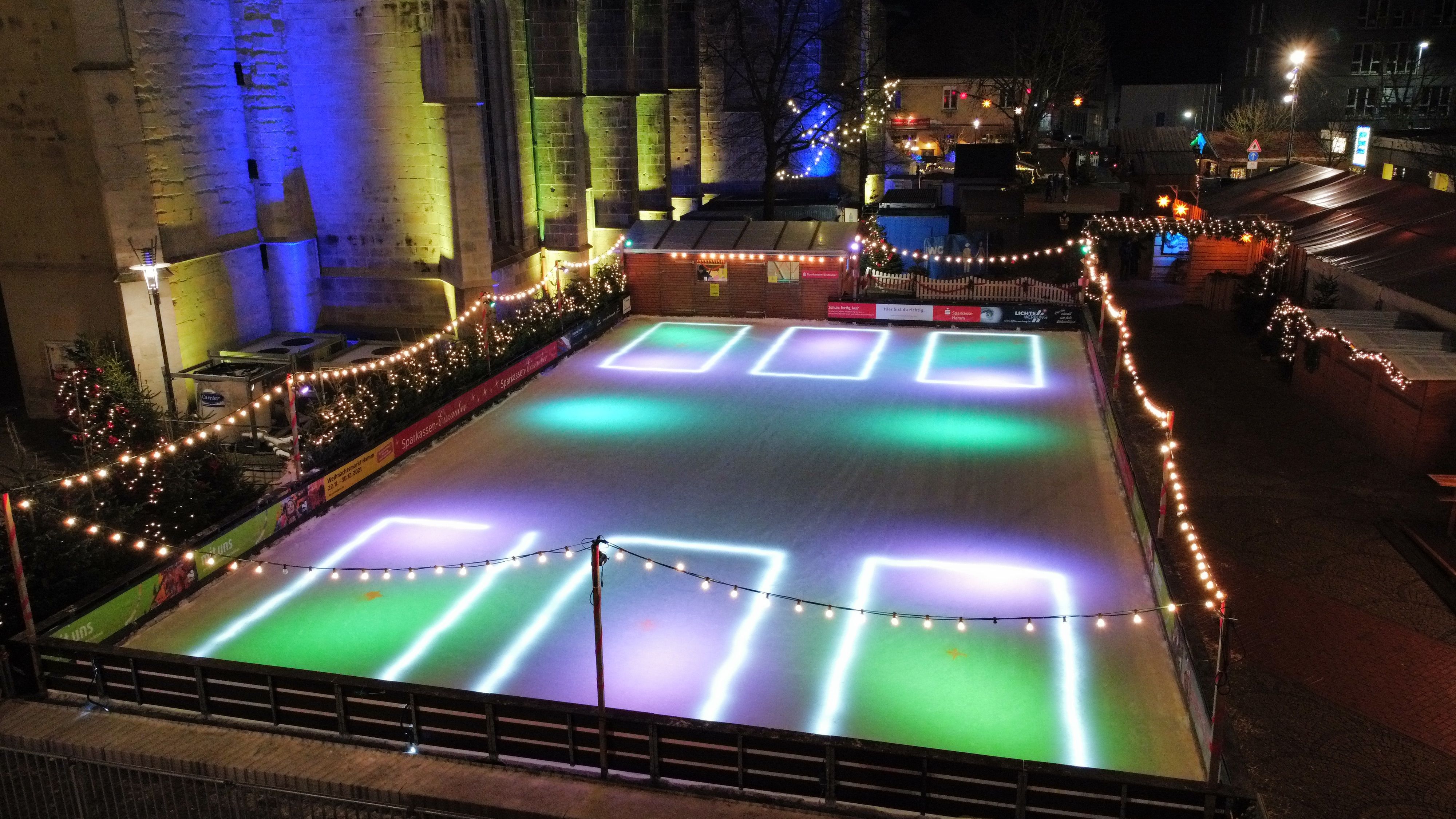 An illuminated ice rink at the Christmas market in Hamm, surrounded by fairy lights and fir trees.