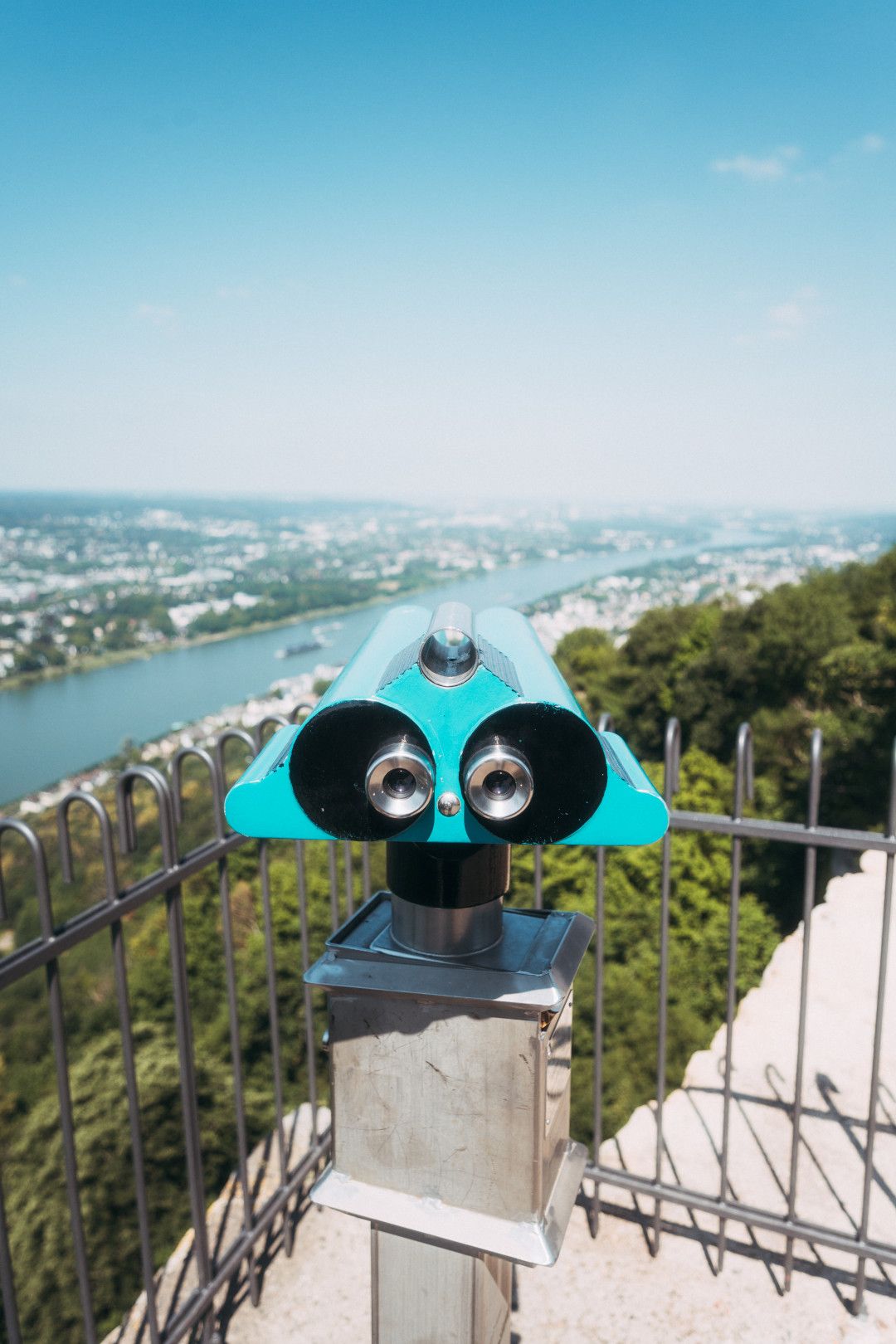 A pair of blue binoculars at a lookout point offers a sweeping view of the Rhine and the green countryside.