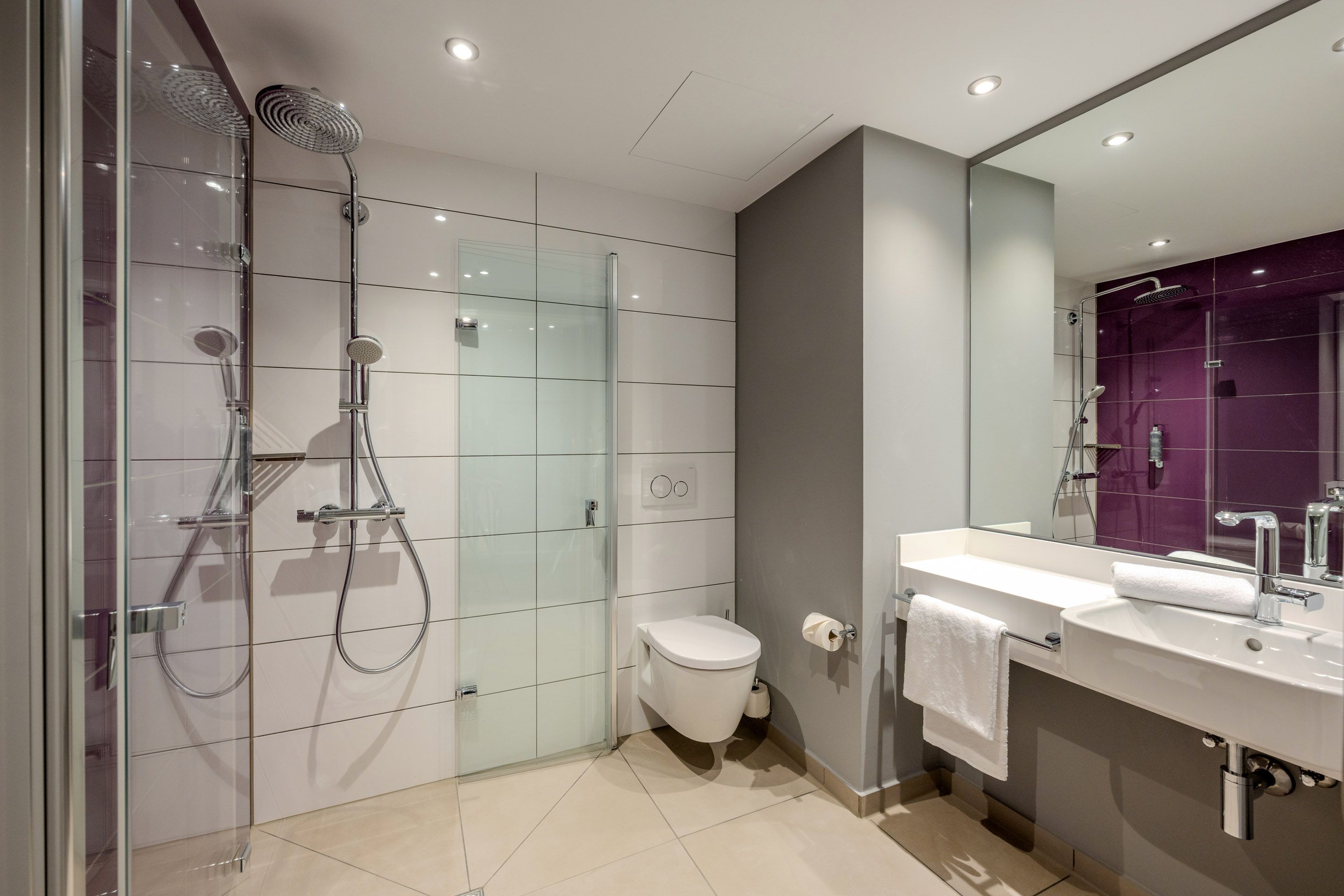 A modern bathroom with a glass shower, a wall-mounted toilet, and a sink with a mirror. The walls are painted white and gray.