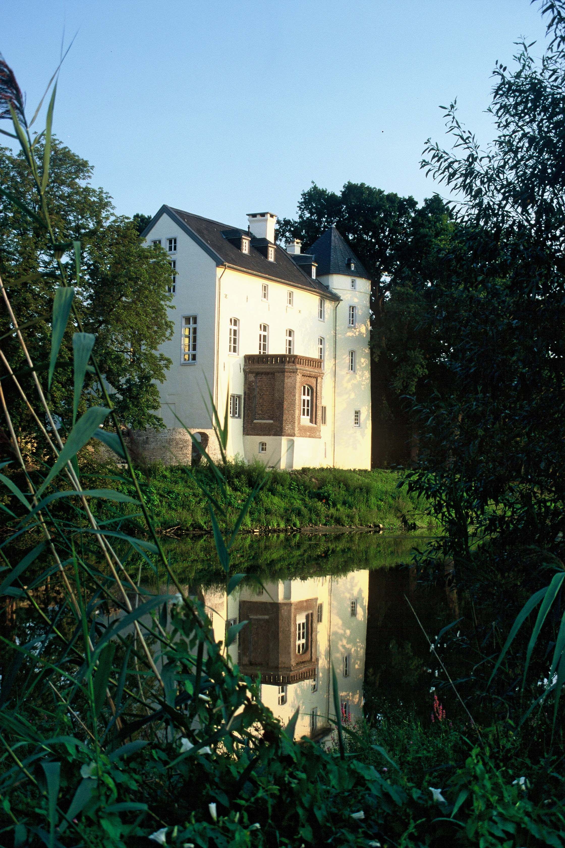 Die weißen Mauern einer kleinen Burg spiegeln sich im Wasser