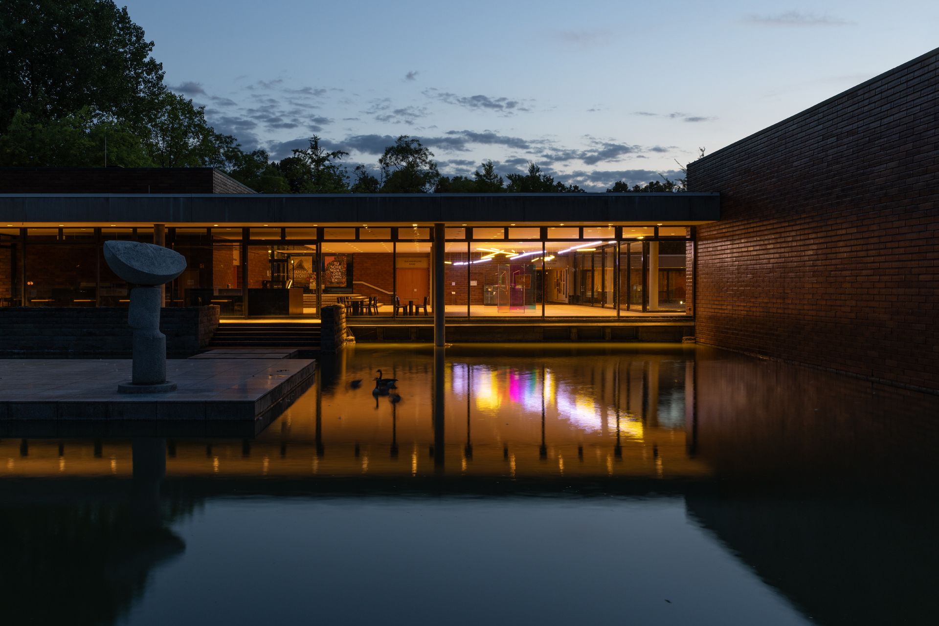 Soft, warm lighting inside the Museum of East Asian Art conveys its serene aesthetic to the outside. Large glass facades offer a view of the Aachener Weiher.