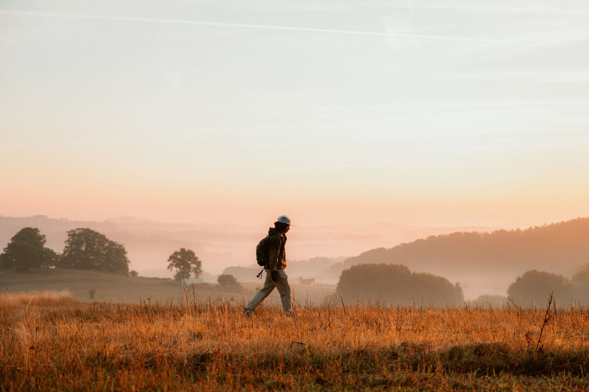 Hikers at sunrise, with fog, trees and fields in the background