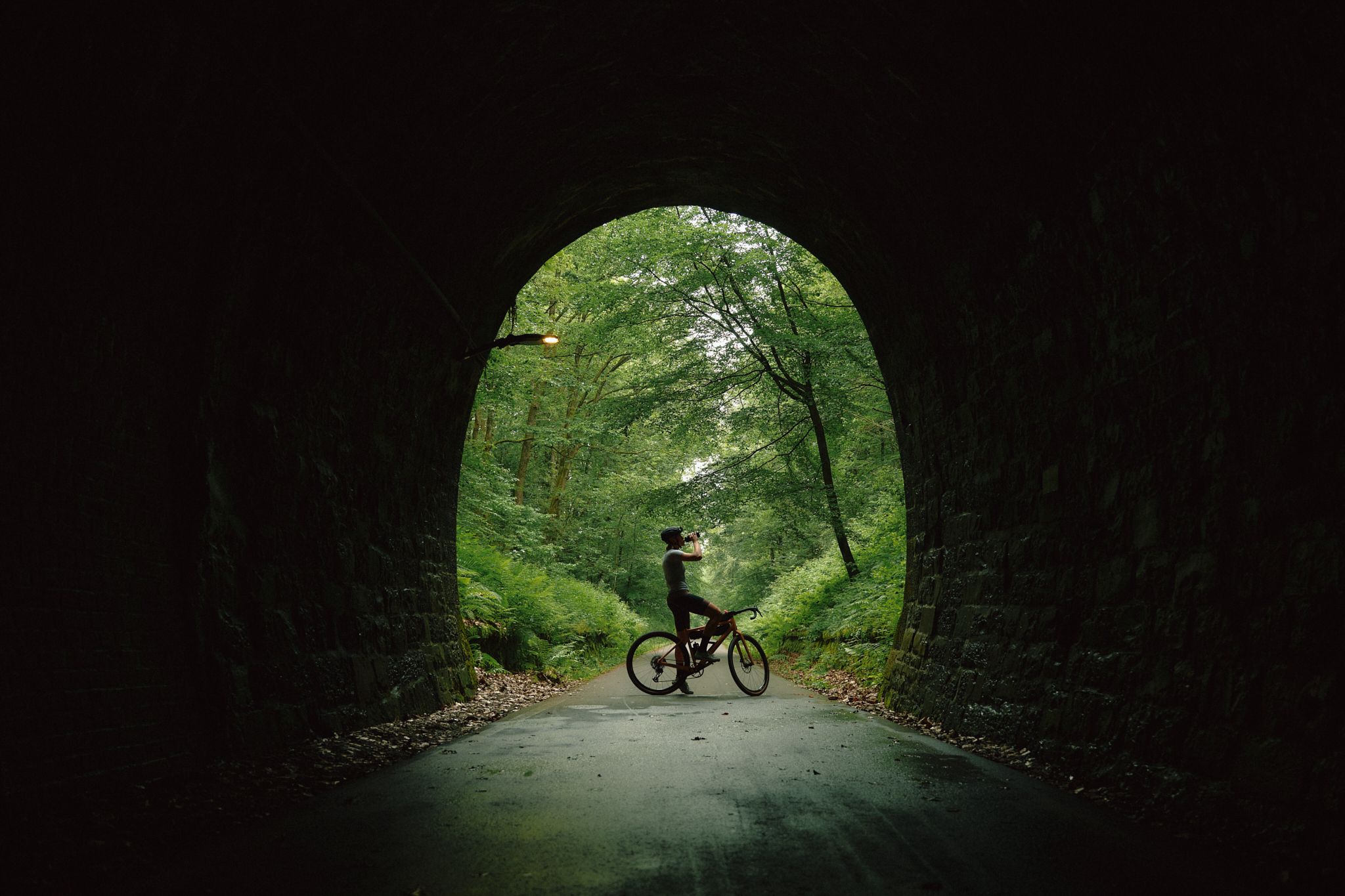 A cyclist stops in a tunnel and drinks from a bottle.