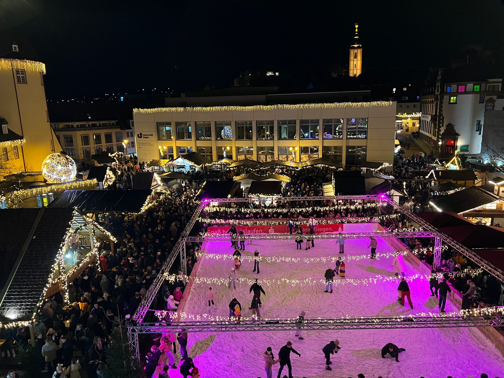The Siegen Christmas market at the Lower Castle features an illuminated ice rink and festively decorated stalls at night.