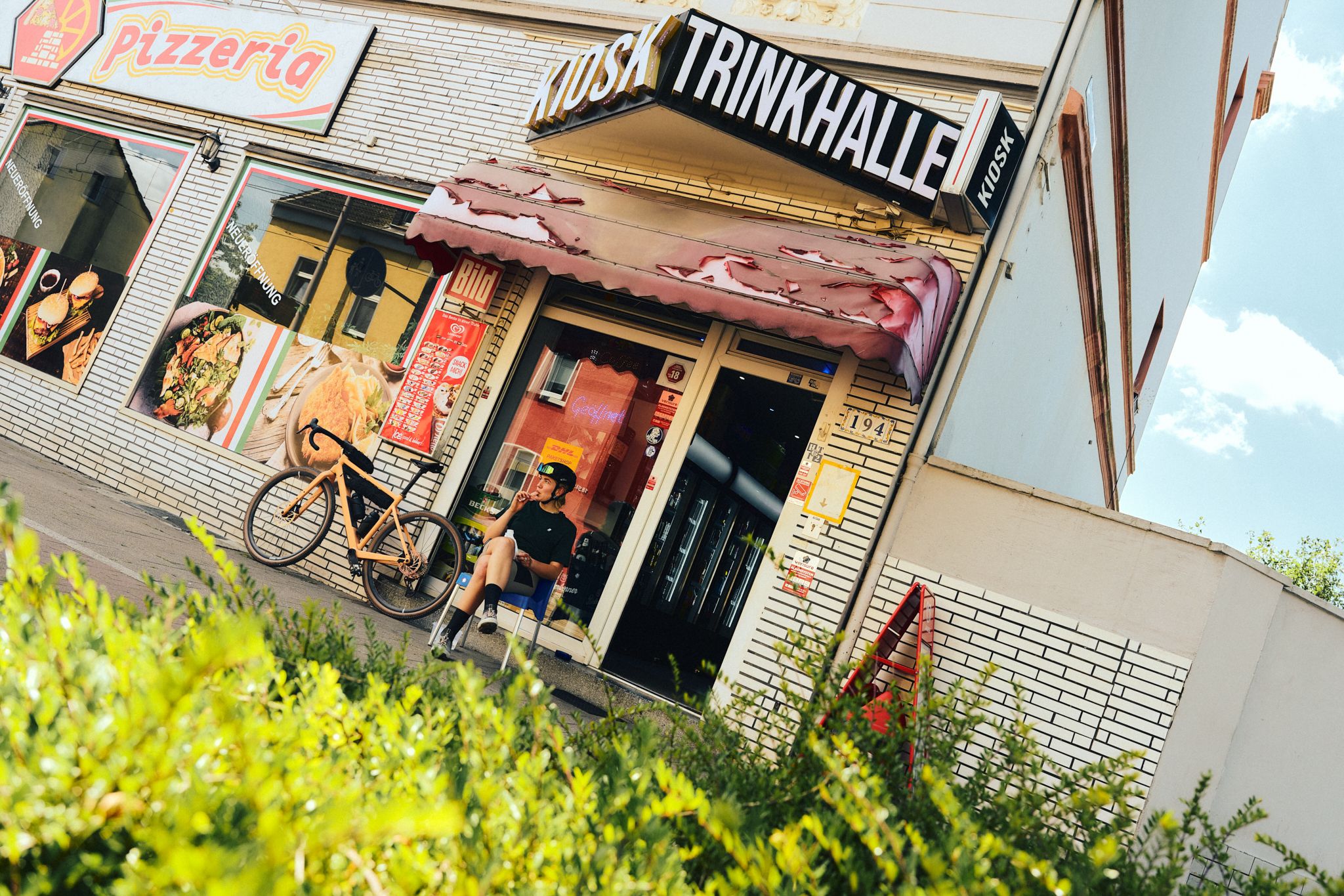 A person is sitting relaxed in front of a refreshment stand in the Ruhr region, next to a bicycle.