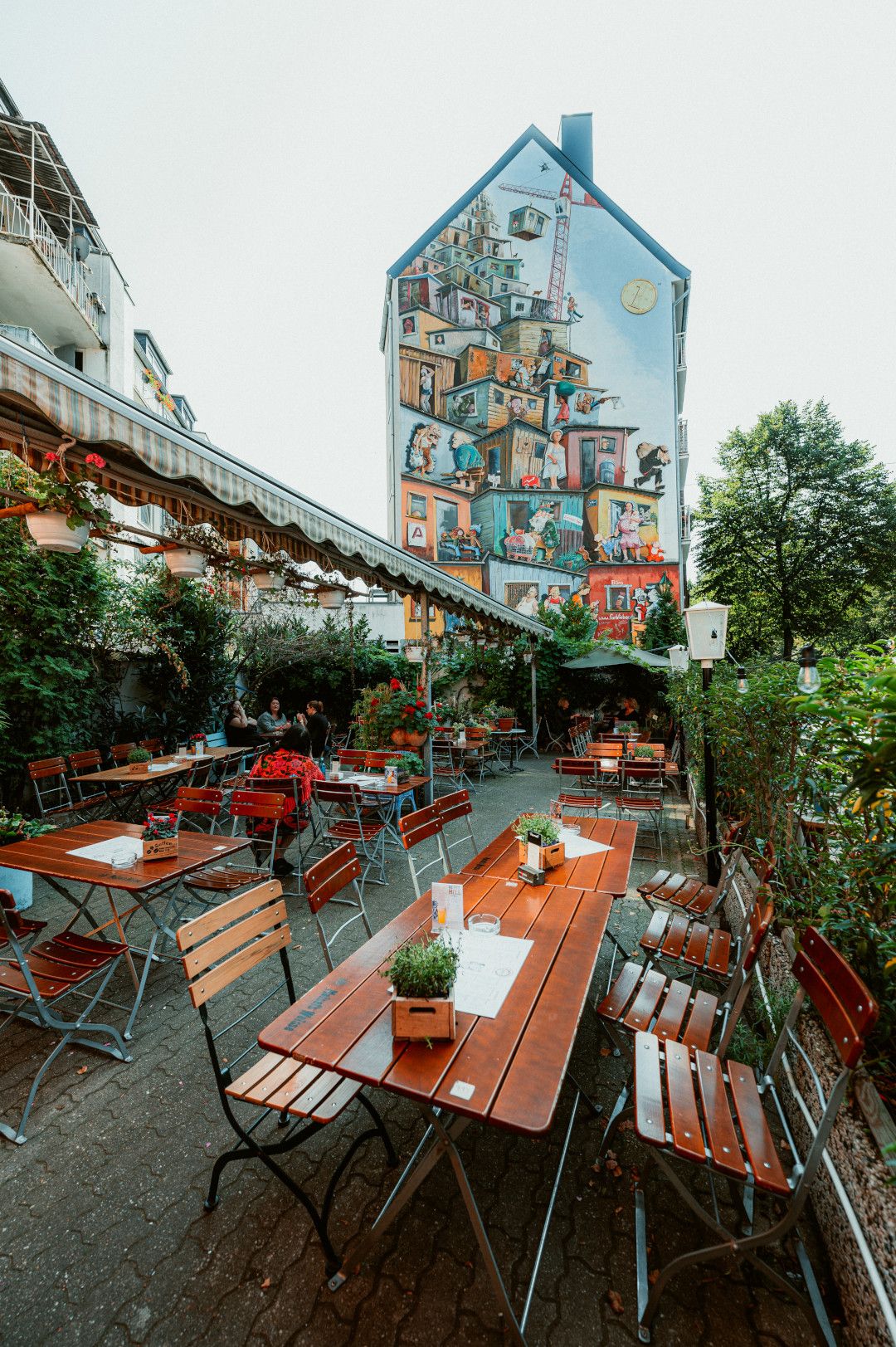 Blick über Holztische und -stühle des Biergarten Tigges hinweg auf Mural 
