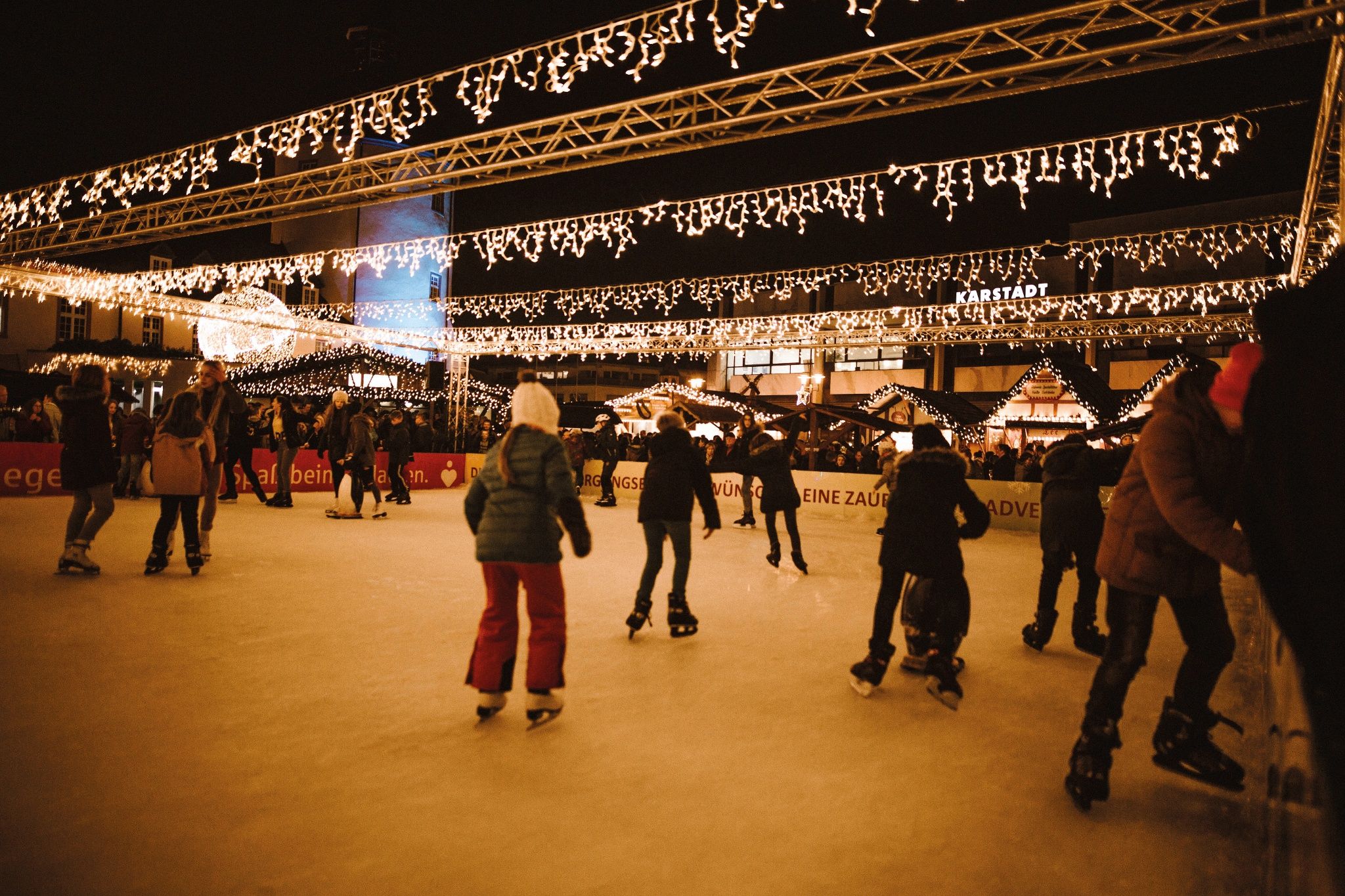 Ice skaters on a festively illuminated ice rink, surrounded by Christmas market stalls and fairy lights.