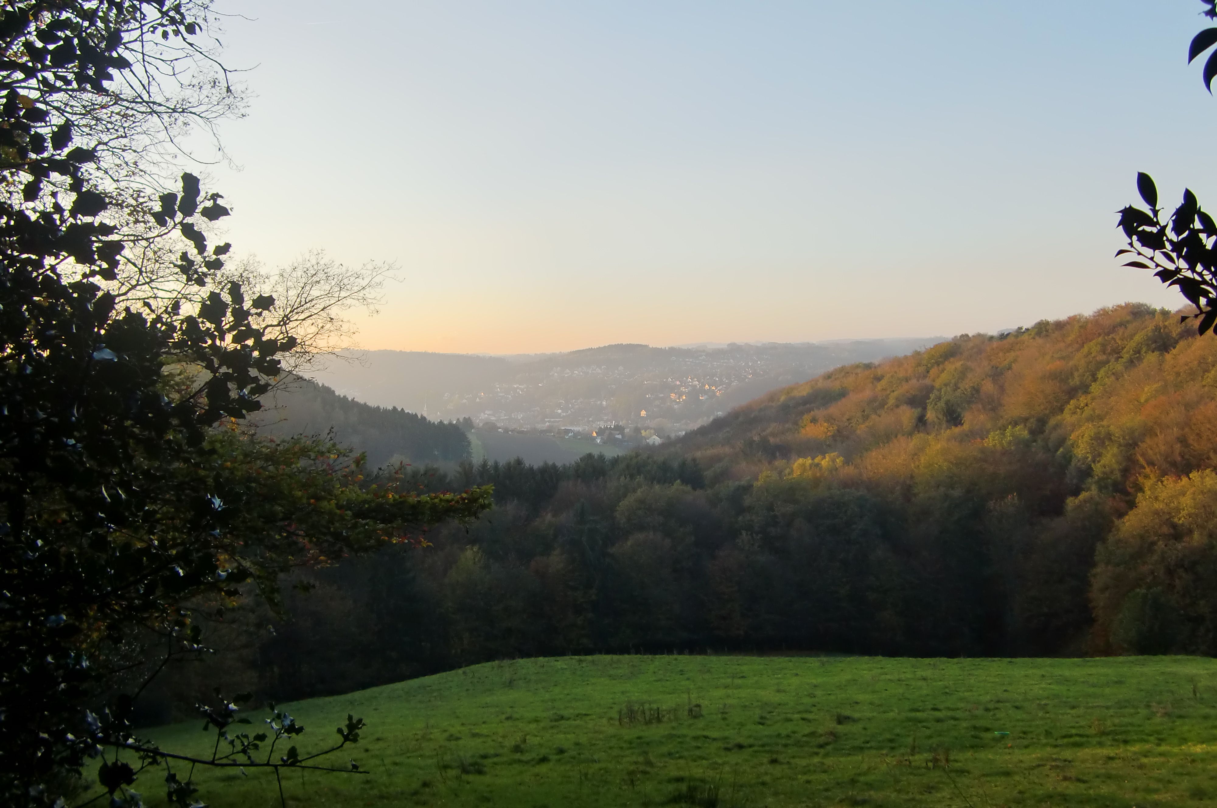 Autumn landscape in the Bergisches Land with green meadows, wooded hills and a village in the background.