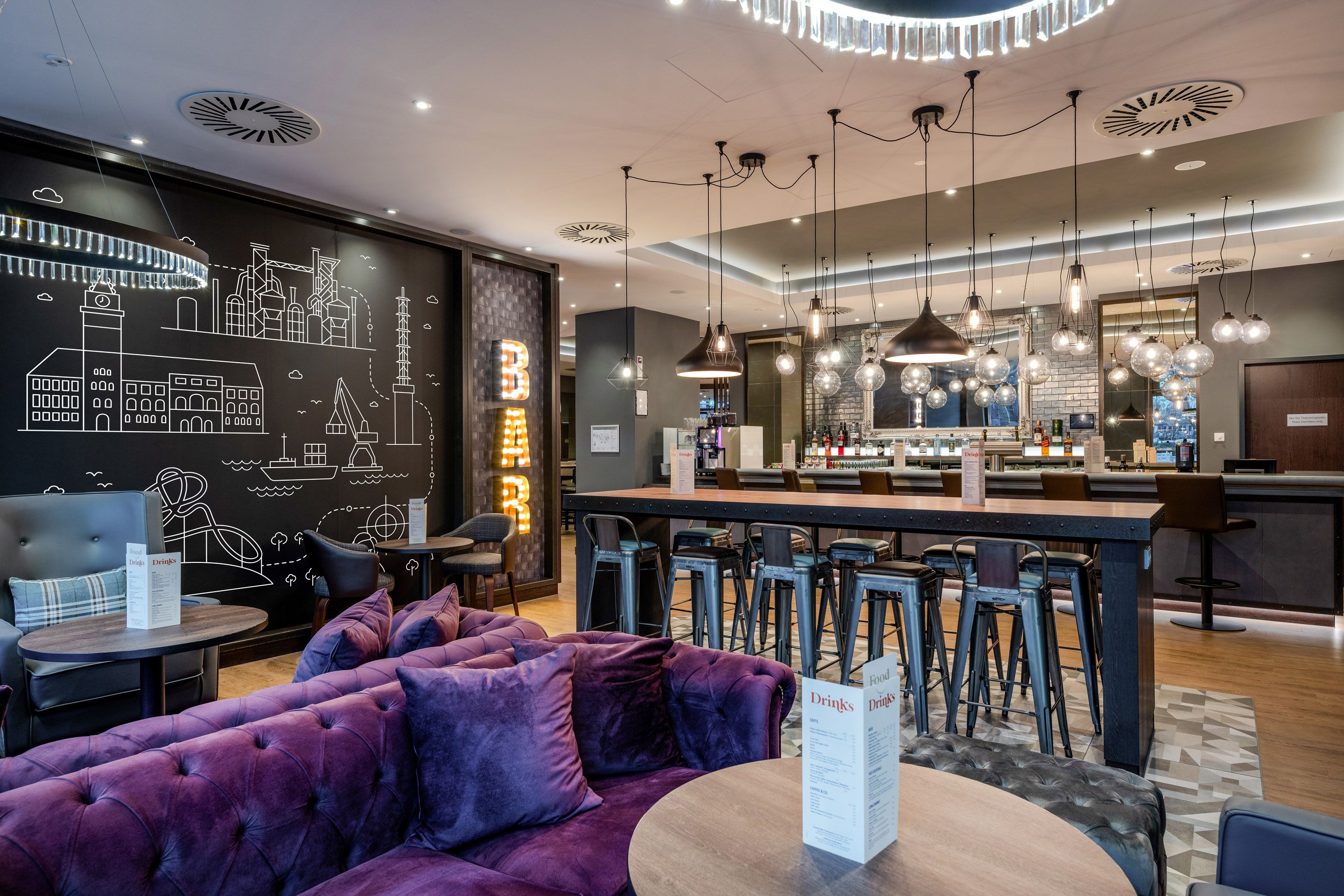 A stylish bar with purple sofas, tall stools, and modern pendant lights. On the wall is a drawing of a cityscape.