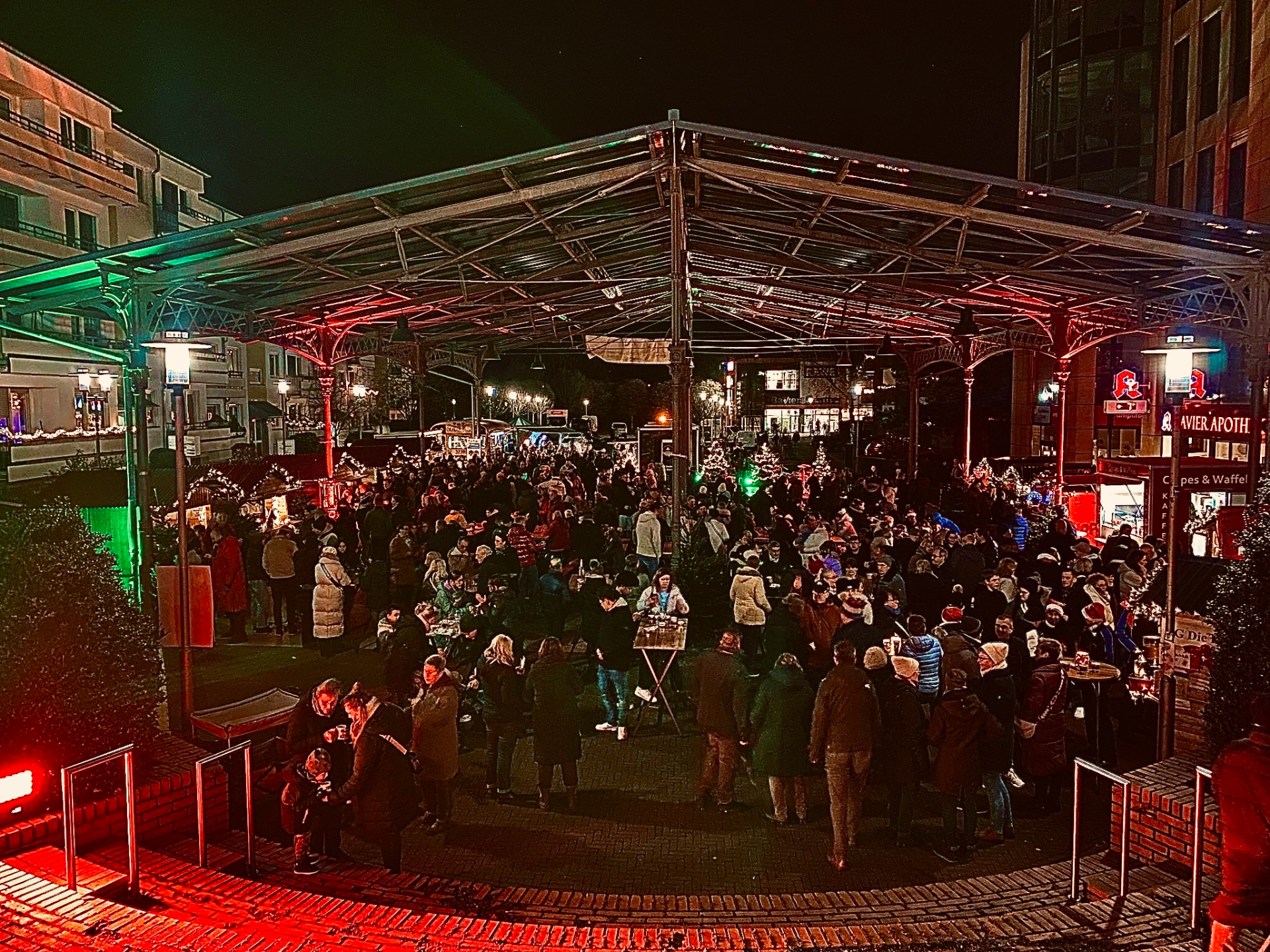 People enjoy the Erkrath Feierabendmarkt - Christmas Edition under an illuminated canopy at night.