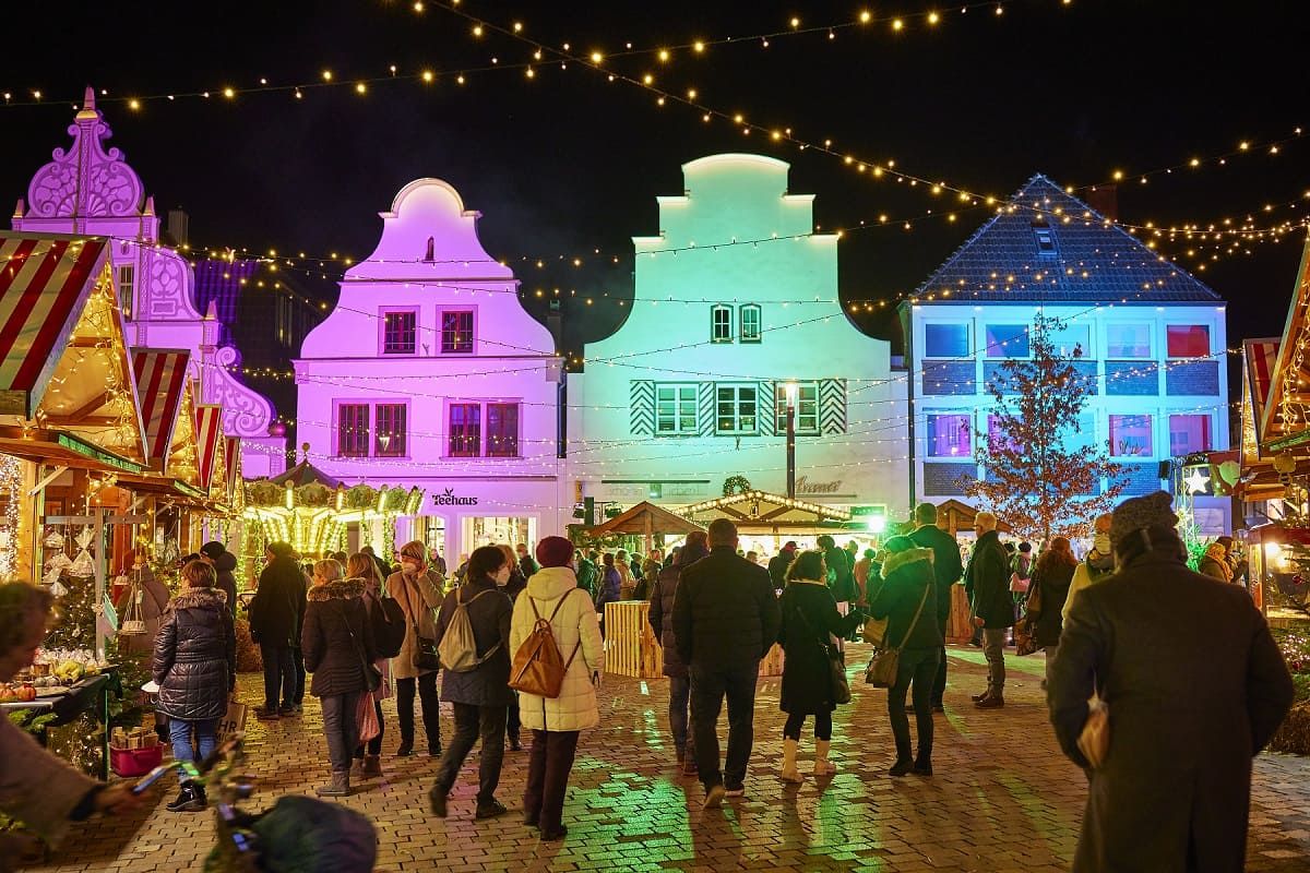 Festively illuminated St. Nicholas market in Burgsteinfurt at night. People stroll between stalls, colorful lights illuminate buildings and create a festive atmosphere.