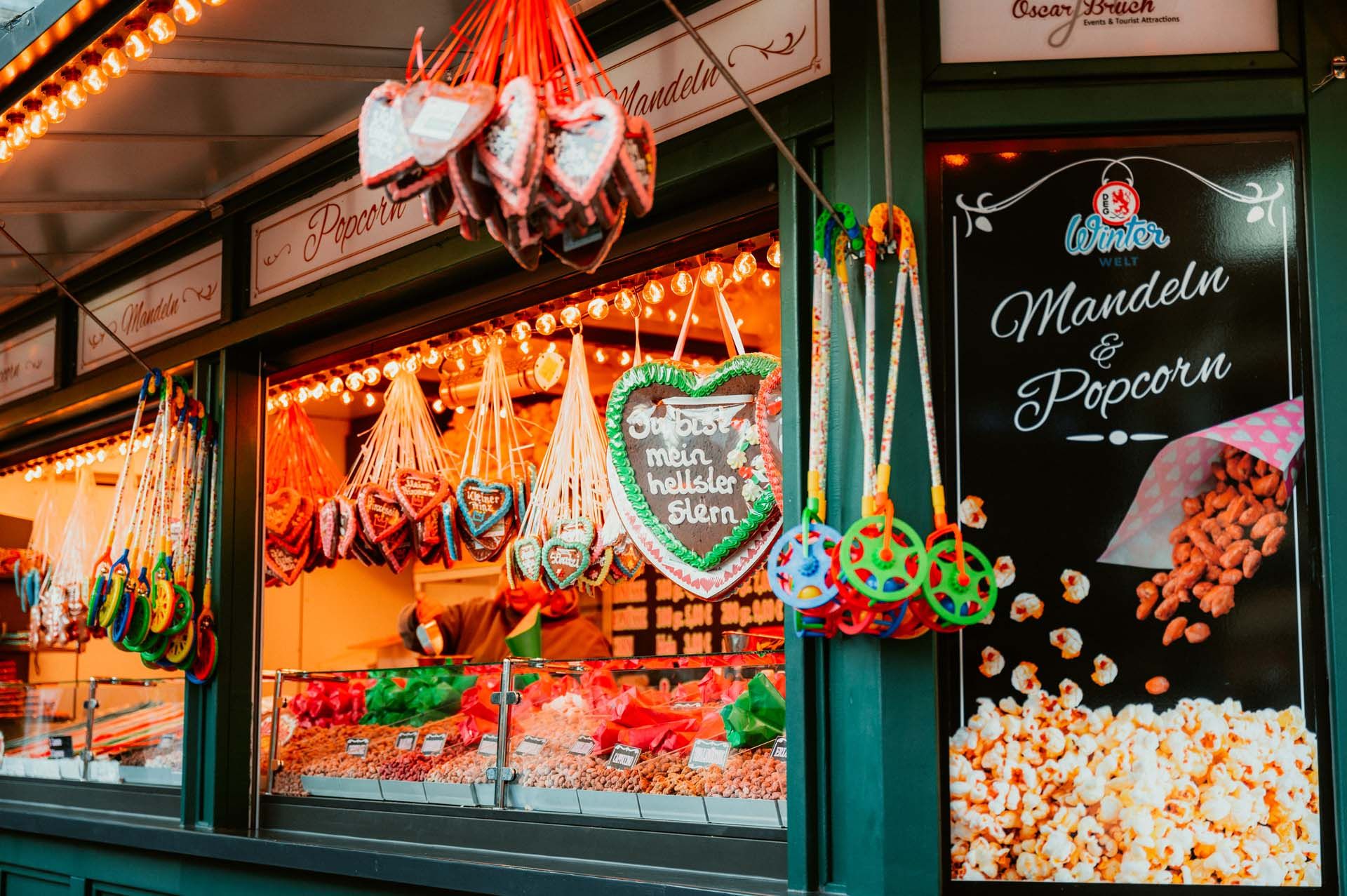 A Christmas market stall with gingerbread hearts, nuts and popcorn. Colorful lights and decorations create a festive atmosphere.
