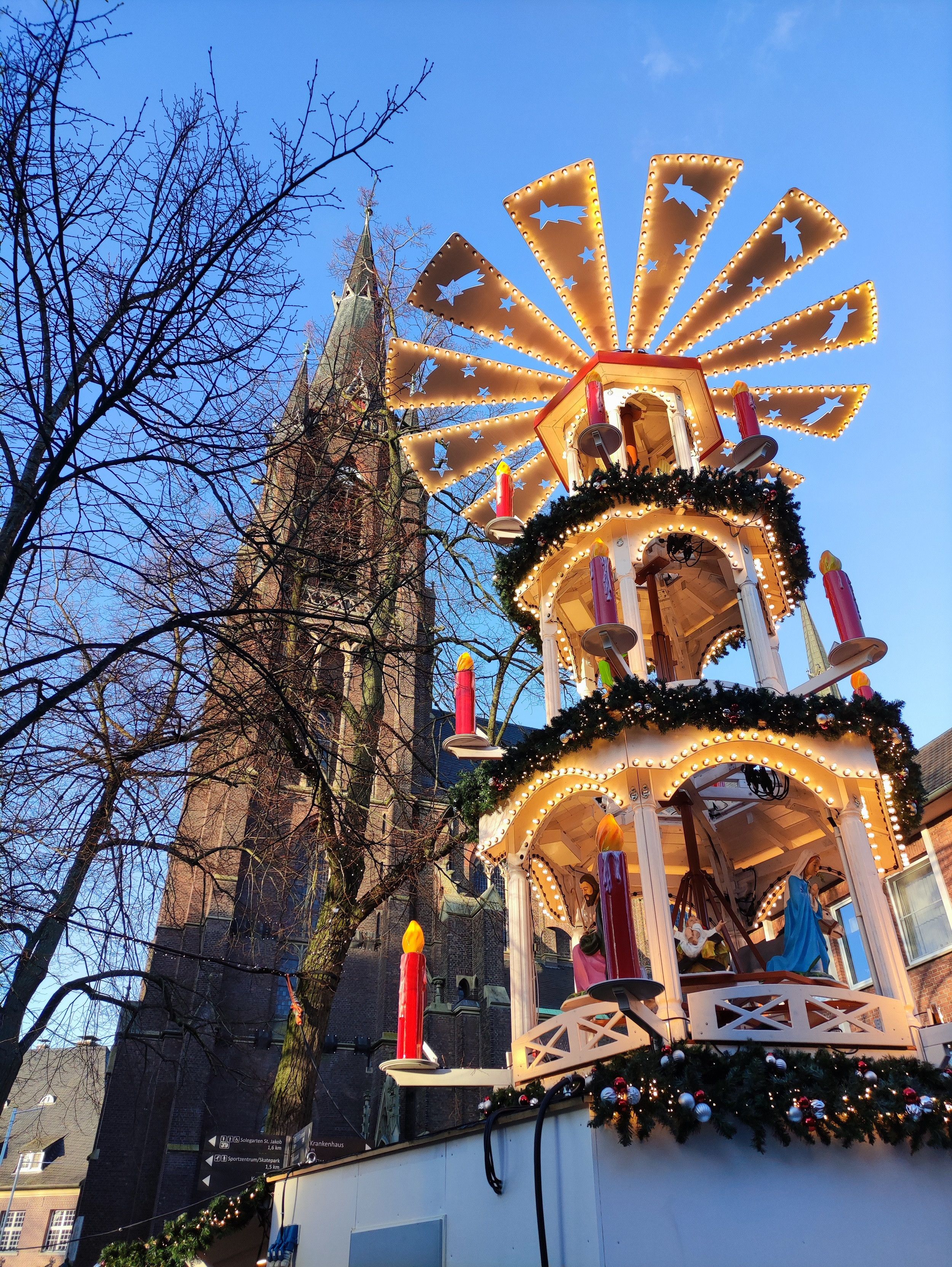 An illuminated Christmas pyramid with figures stands in front of a high church tower façade in Kevelaer and heralds the Christmas spirit.