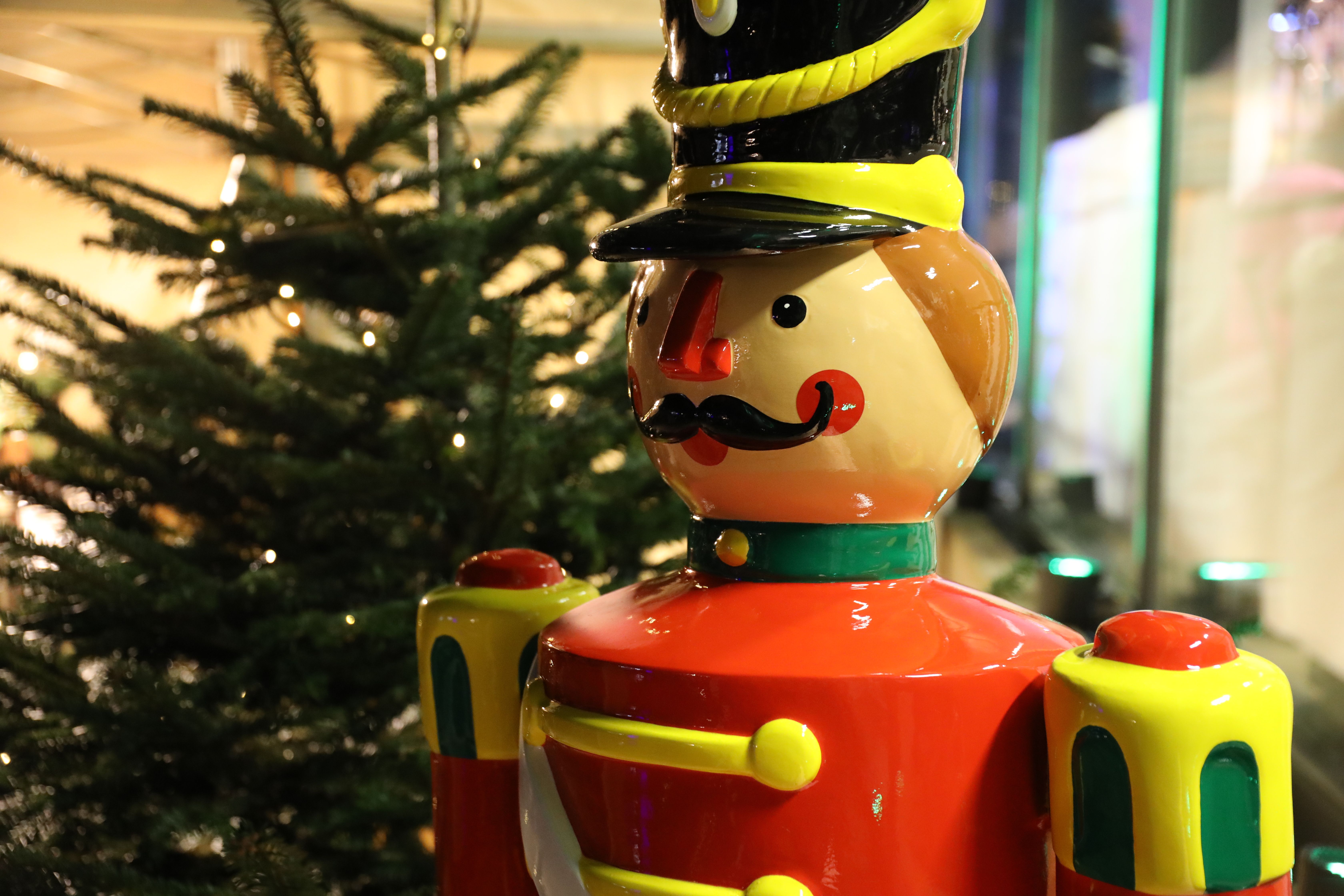 A colorful nutcracker stands in front of an illuminated Christmas tree.
