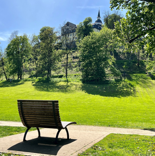 Siegburg Local Recreation: A bench in a sunny park with a view of Siegburg Castle on the hill.