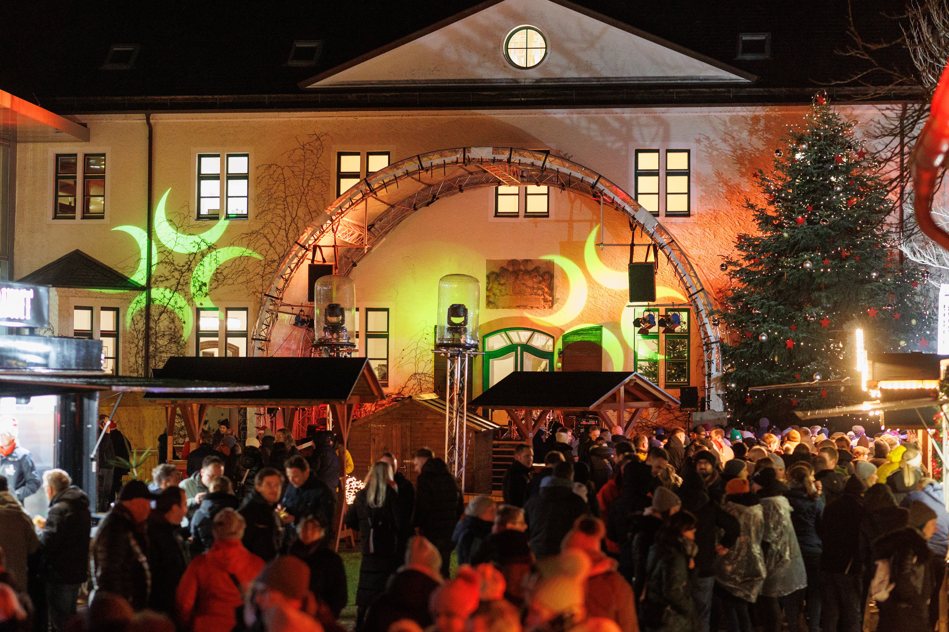 Numerous people, a festively decorated Christmas tree and lovingly designed stalls combine to create an atmospheric ensemble on the brightly lit square.