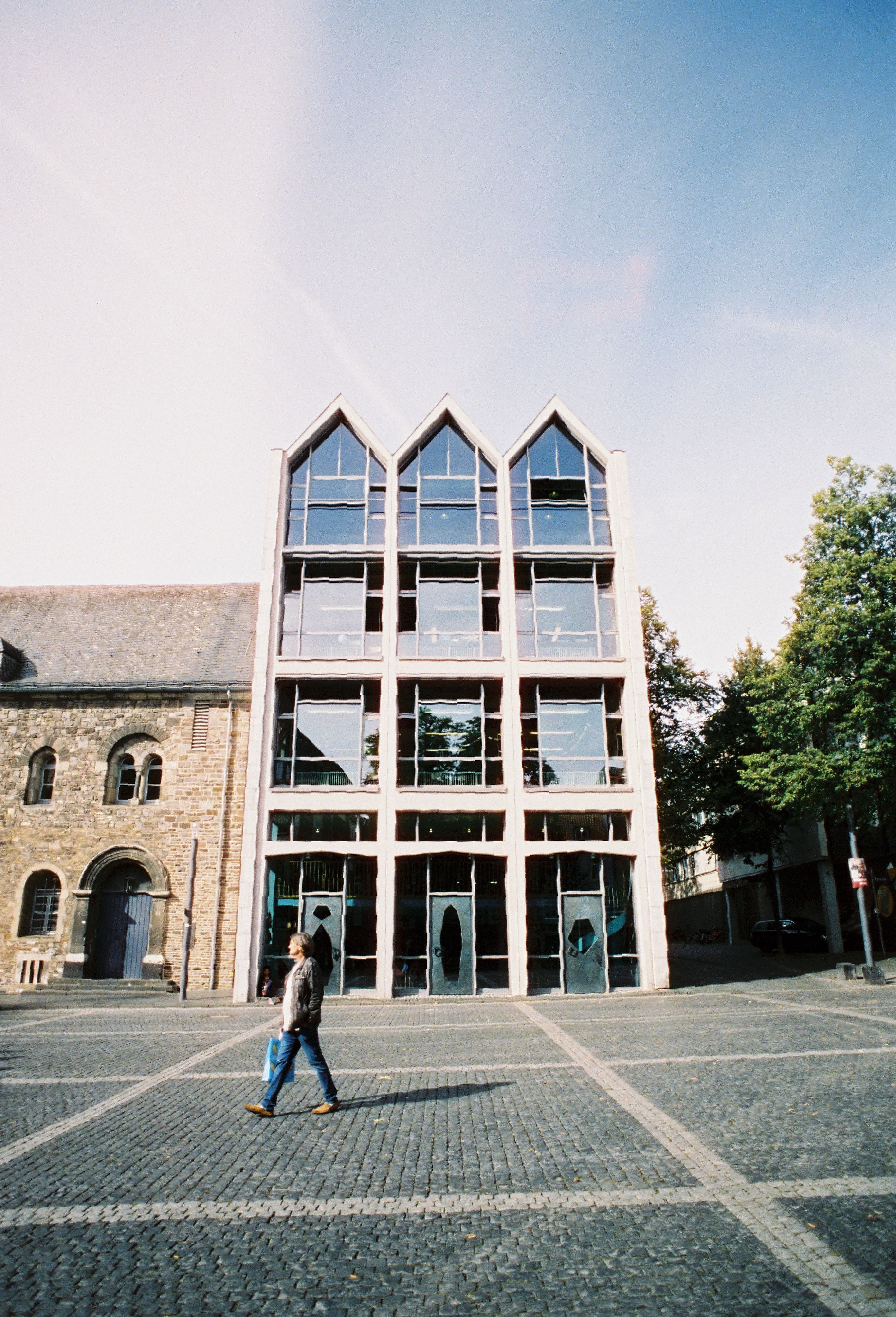 A modern building with a glass facade next to an old stone building in Aachen's Old Town.