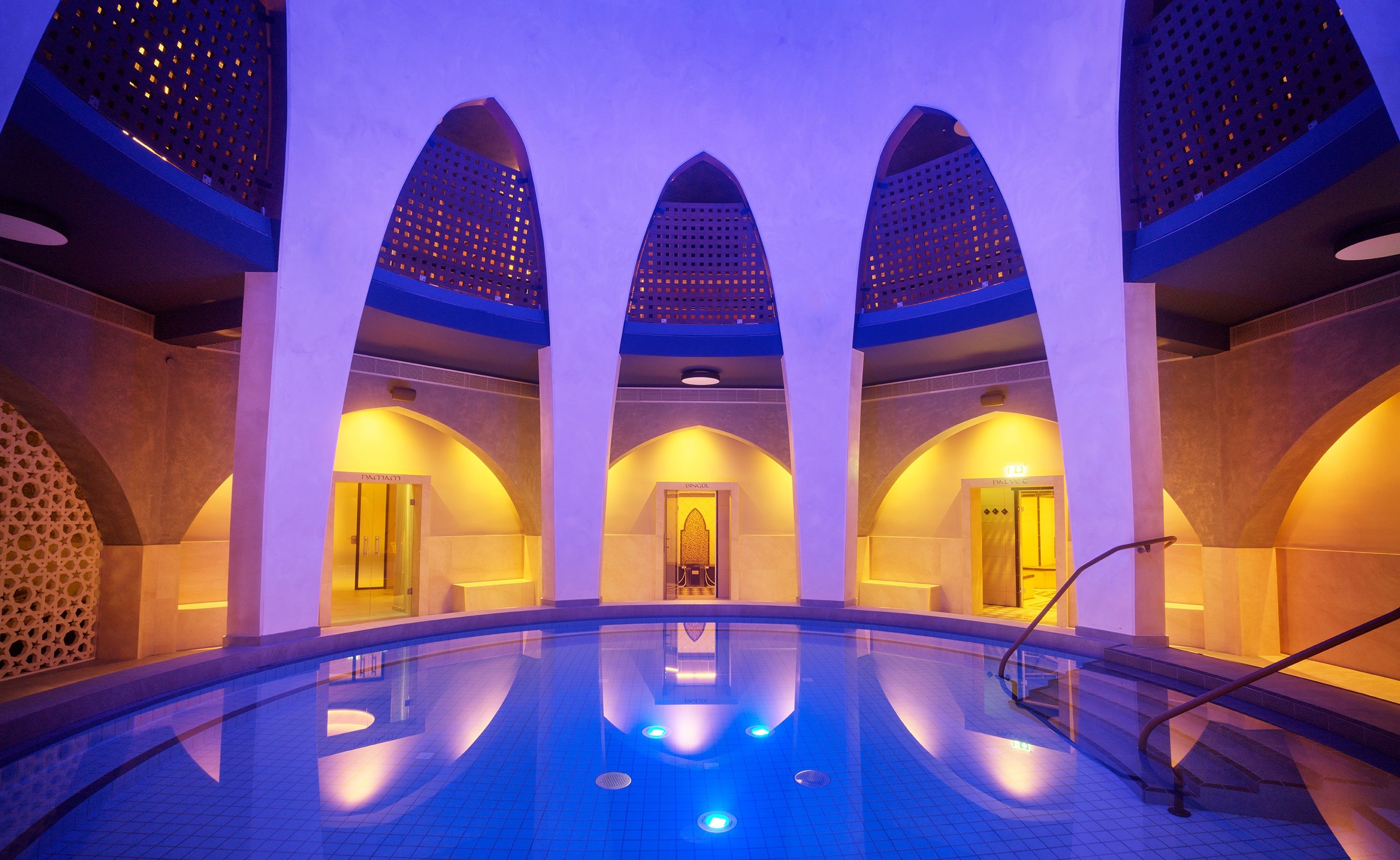The Carolus Therme in Aachen at night with illuminated pool and vaulted ceilings.