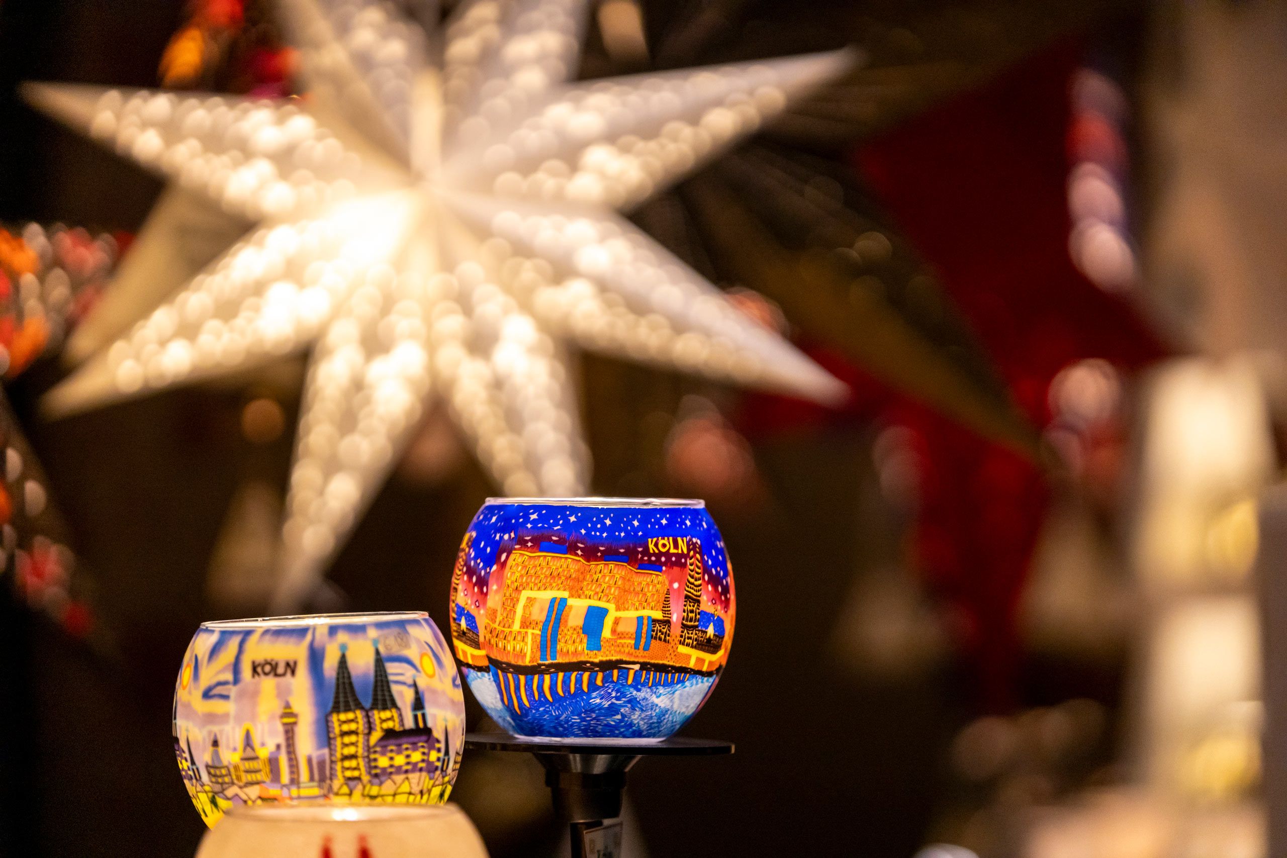 Colourful candle holders with Cologne motifs and a large, bright star in the background create a festive atmosphere at the Market of Angels.