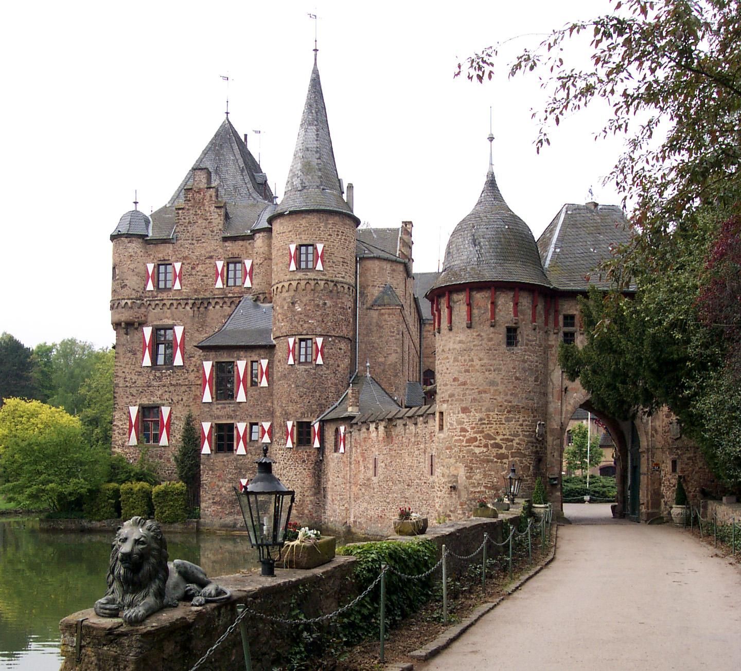 Burg am Wassergraben mit Türmen und rot-weißen Fensterläden