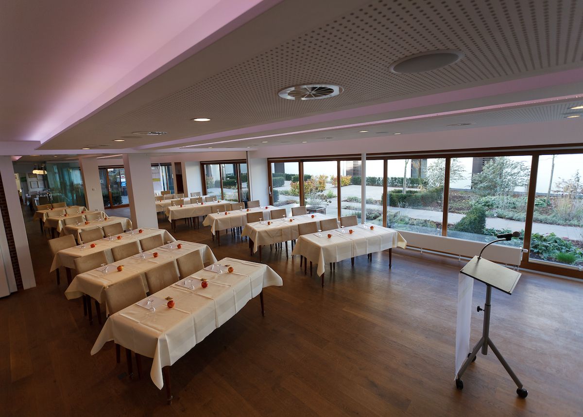The Kalflak 1+2 room in Kalkar with set tables and a lectern, surrounded by large windows overlooking a garden.