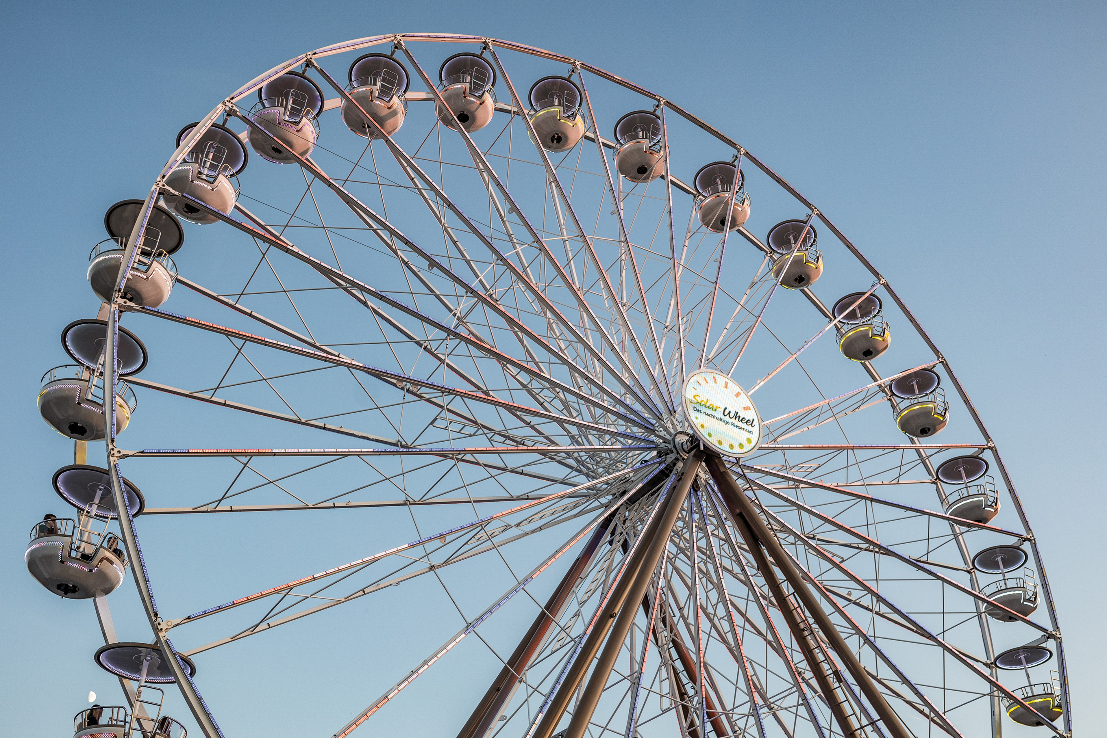 The "Solar Wheel" Ferris wheel, with its illuminated gondolas, stands out against the blue sky.
