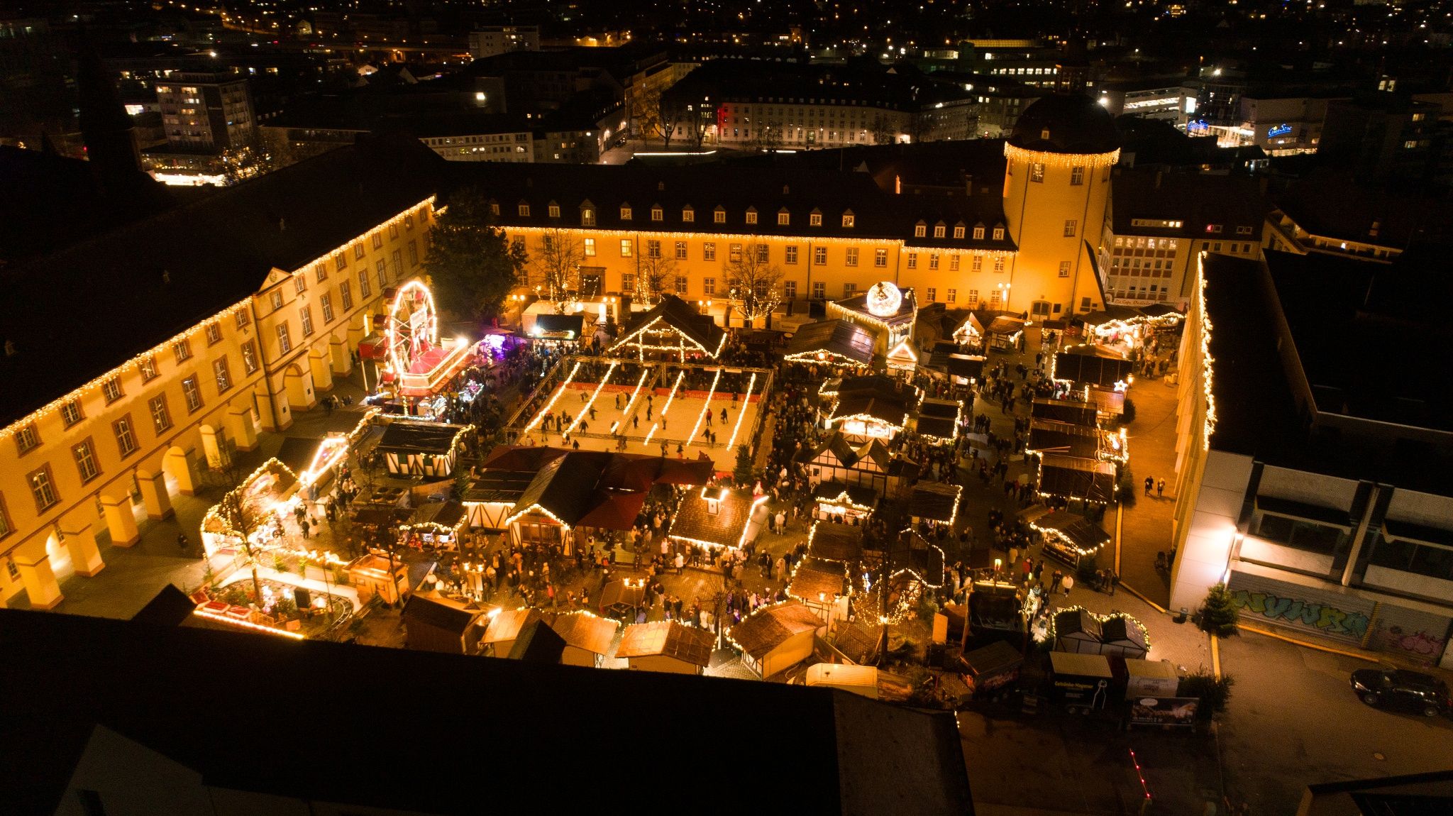 Aerial view of the Siegen Christmas market at the Lower Castle. The market is festively illuminated, with an ice rink and numerous stalls.