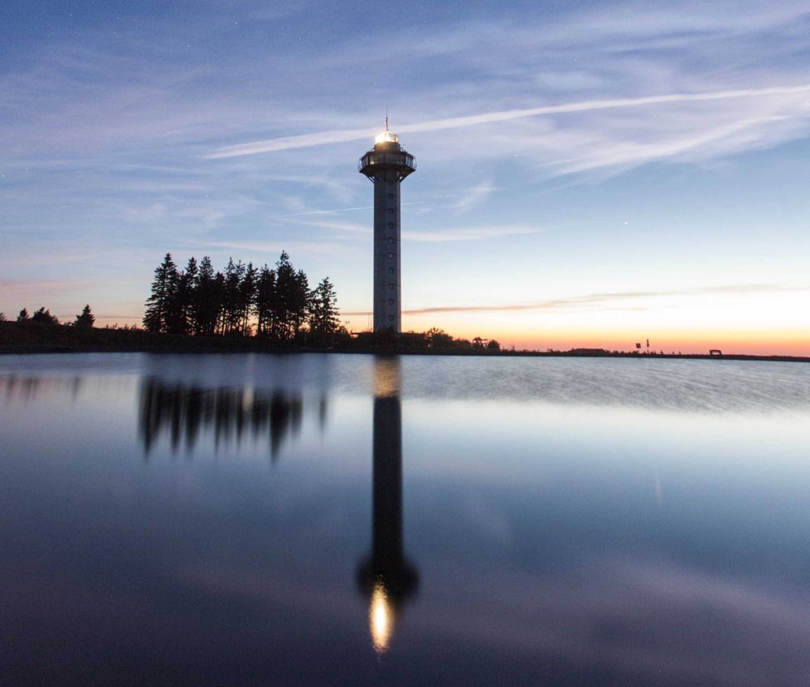 The Hochheideturm is reflected in the calm Ettelsberg mountain lake at sunset.