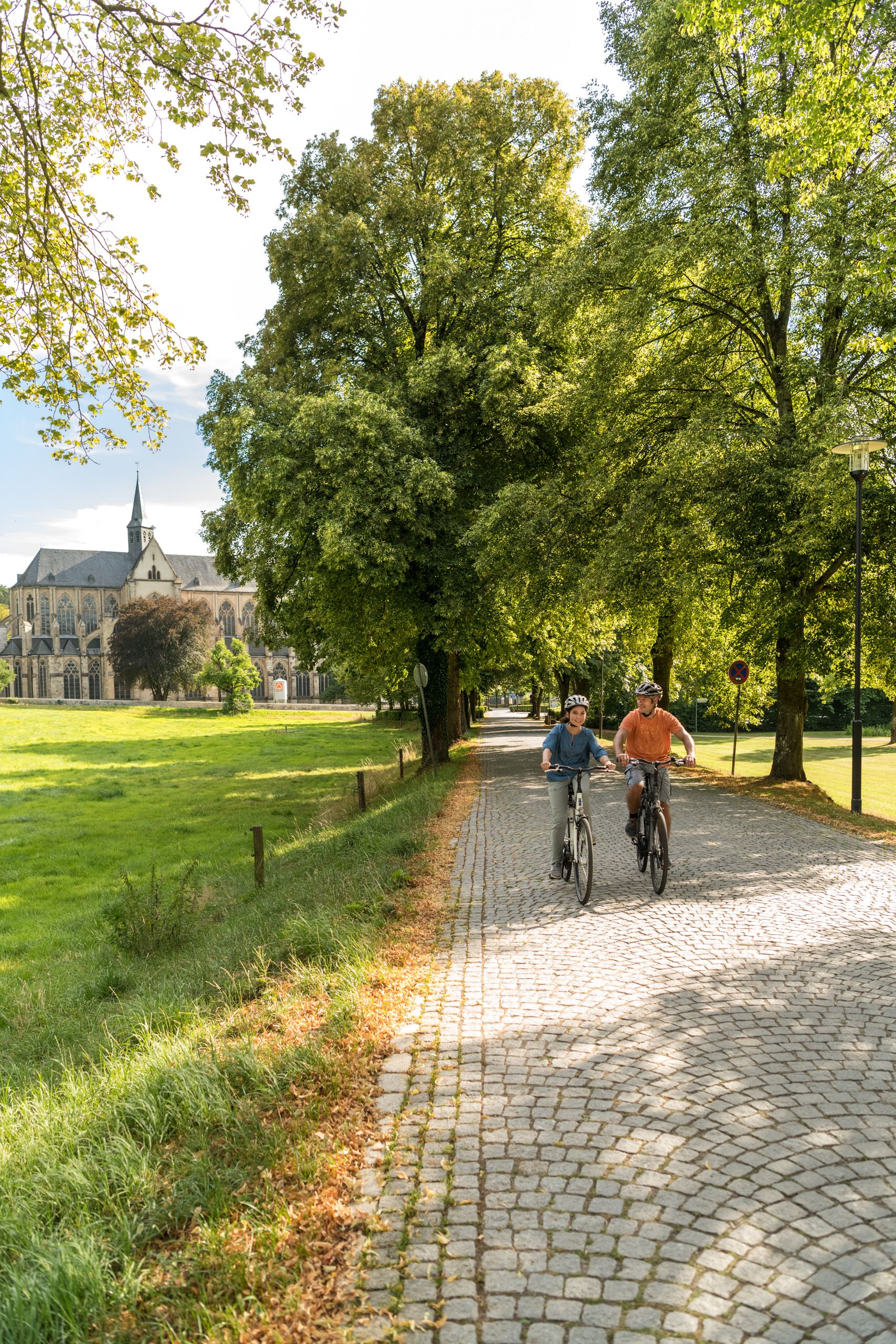 Two cyclists on a paved path. Altenberg Cathedral in the background.