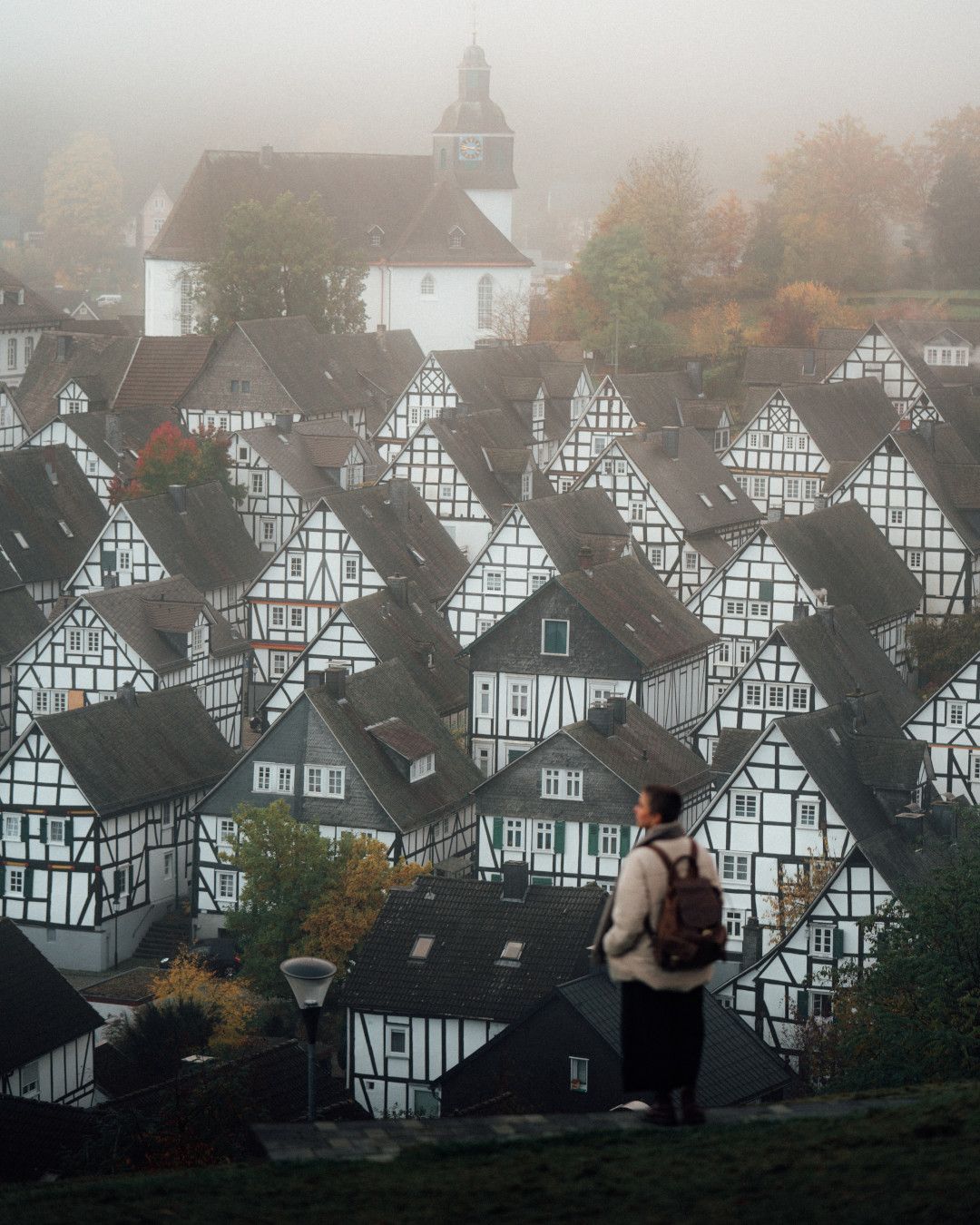 Frau mit Rucksack schaut auf Fachwerkort, der im Nebel zu ihren Füßen liegt