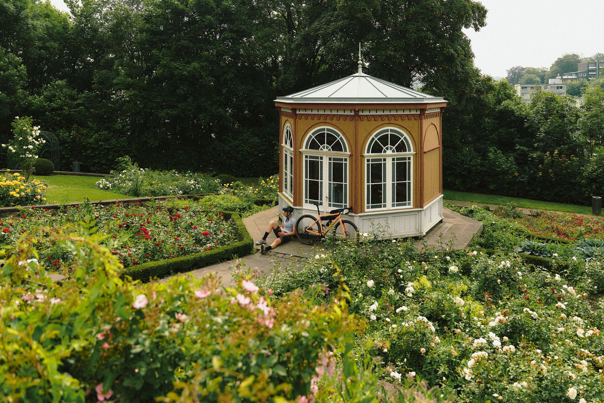 A cyclist is resting next to a gazebo in a garden full of flowers.