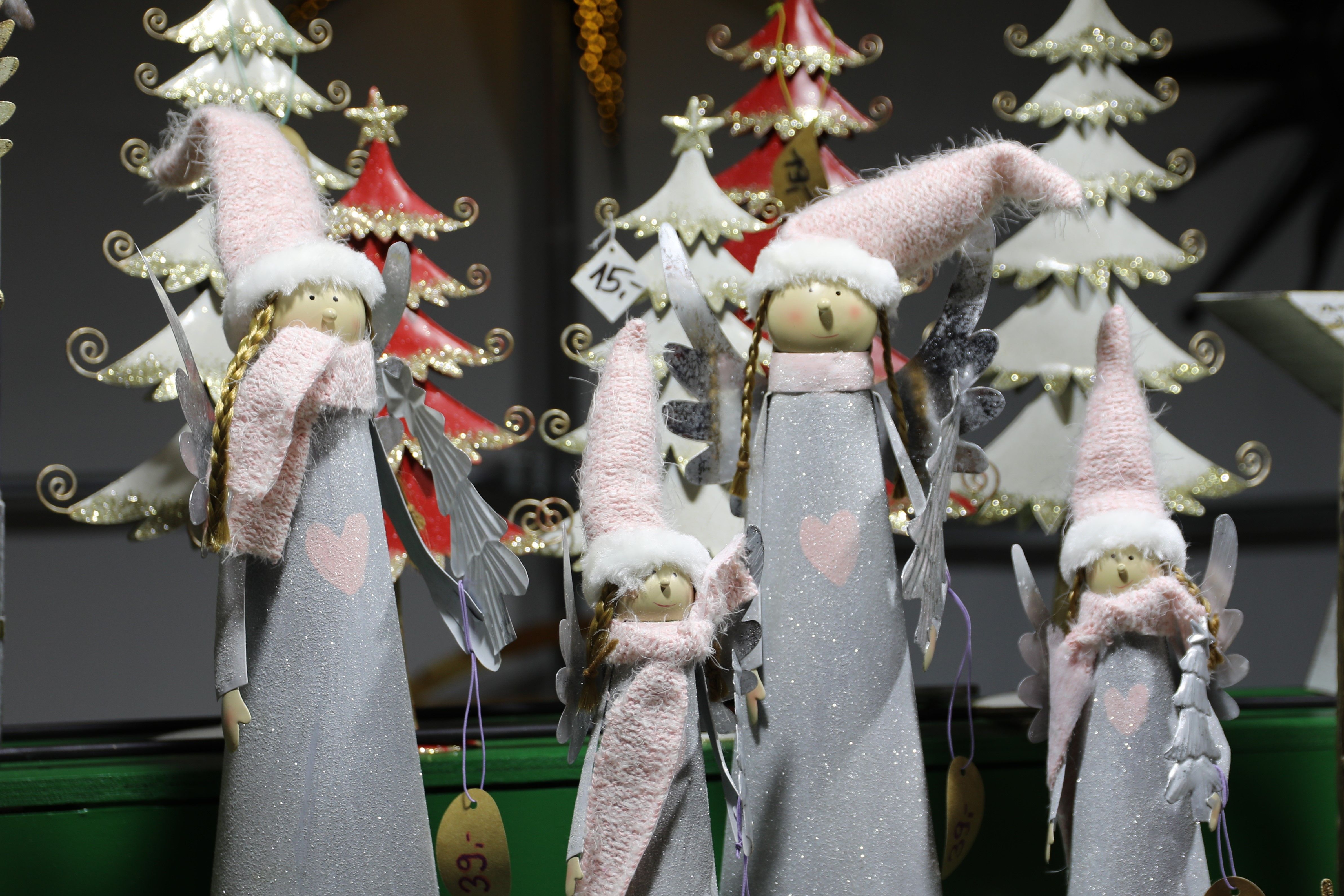 Christmas figures with pink hats and scarves stand in front of decorative Christmas trees.